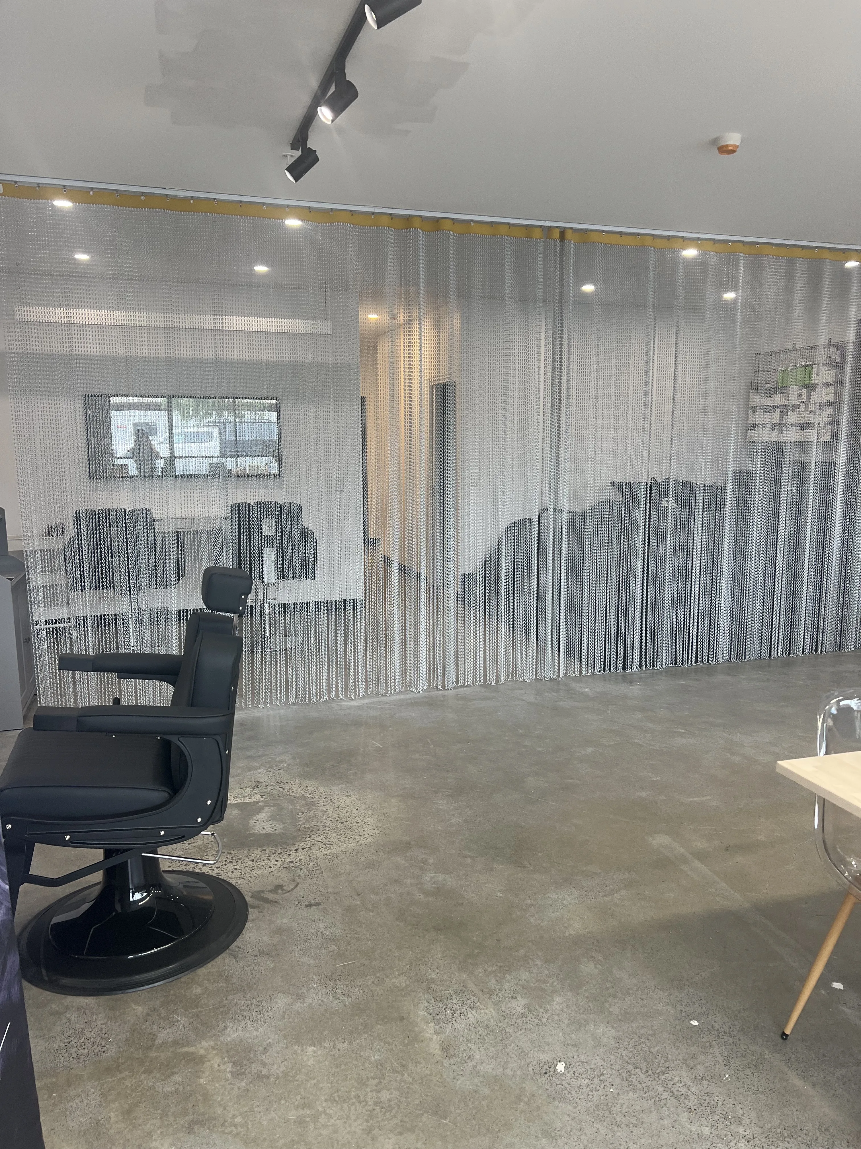 Tone Salon room view — black styling chair against the signature chainmail wall with retail rack