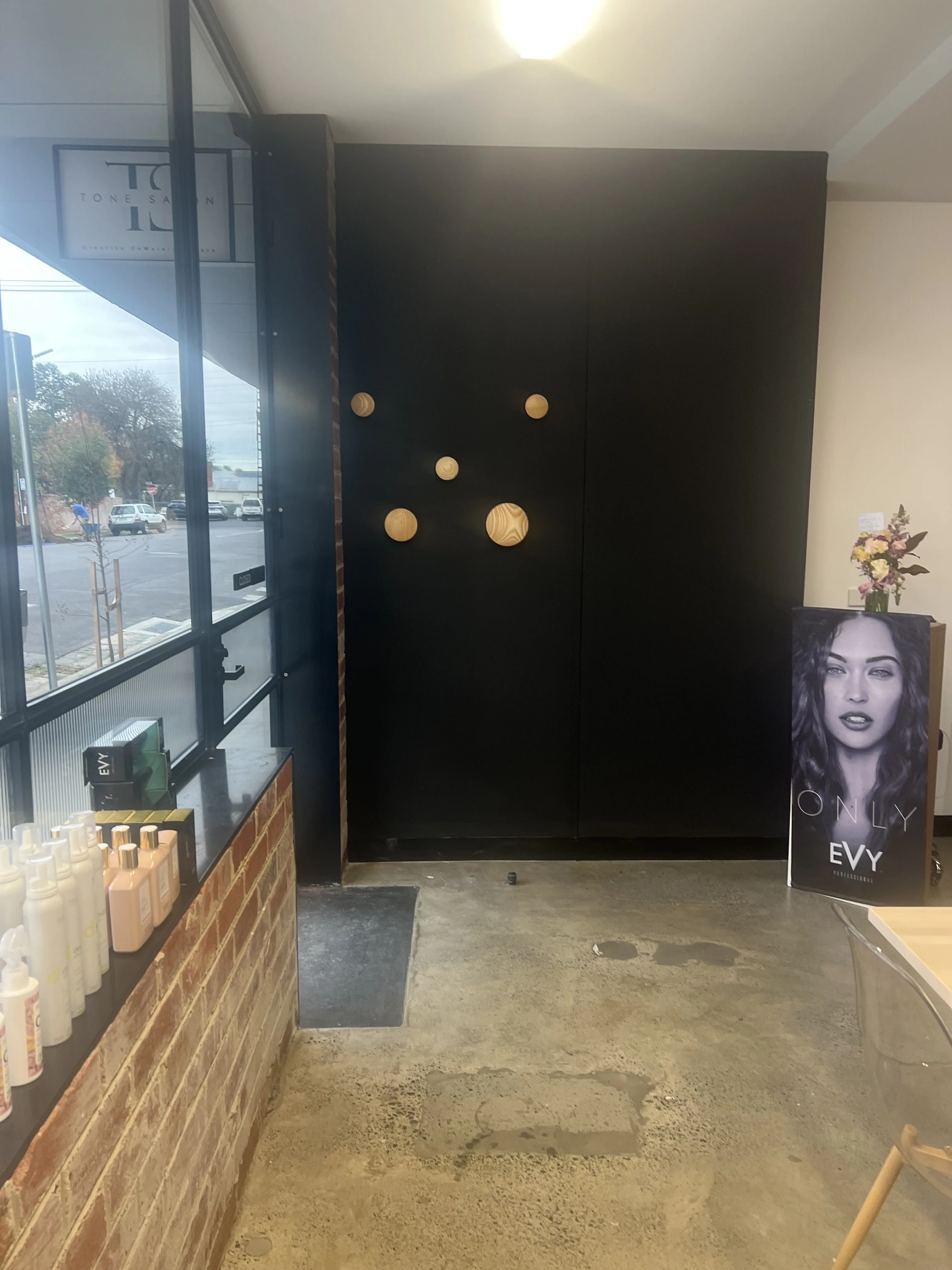 Tone Salon shopfront on Simpson St — window wordmark, EVY retail shelf, black feature wall with timber discs