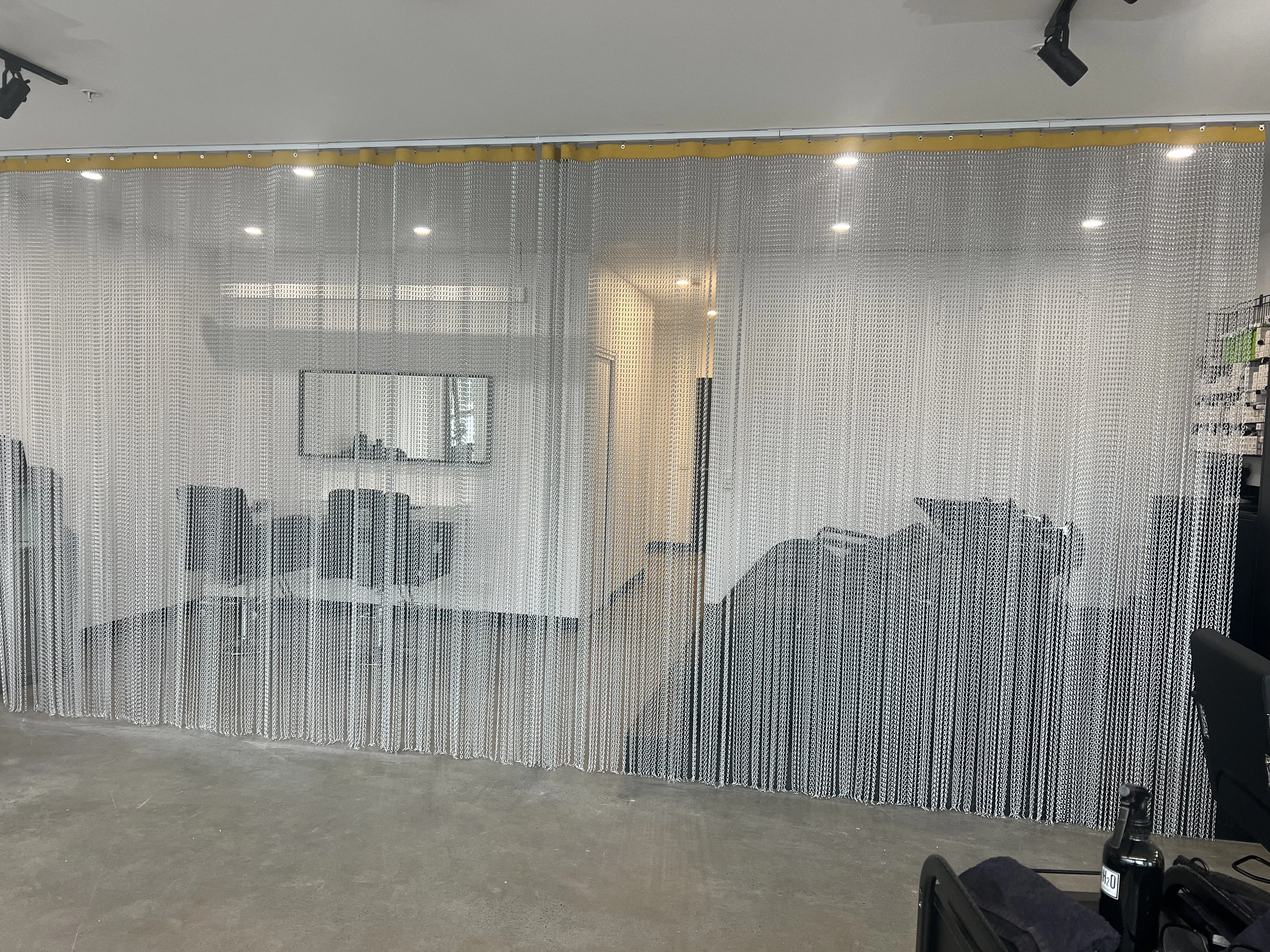 Tone Salon chainmail curtain parting, a lit corridor receding through the silver mesh
