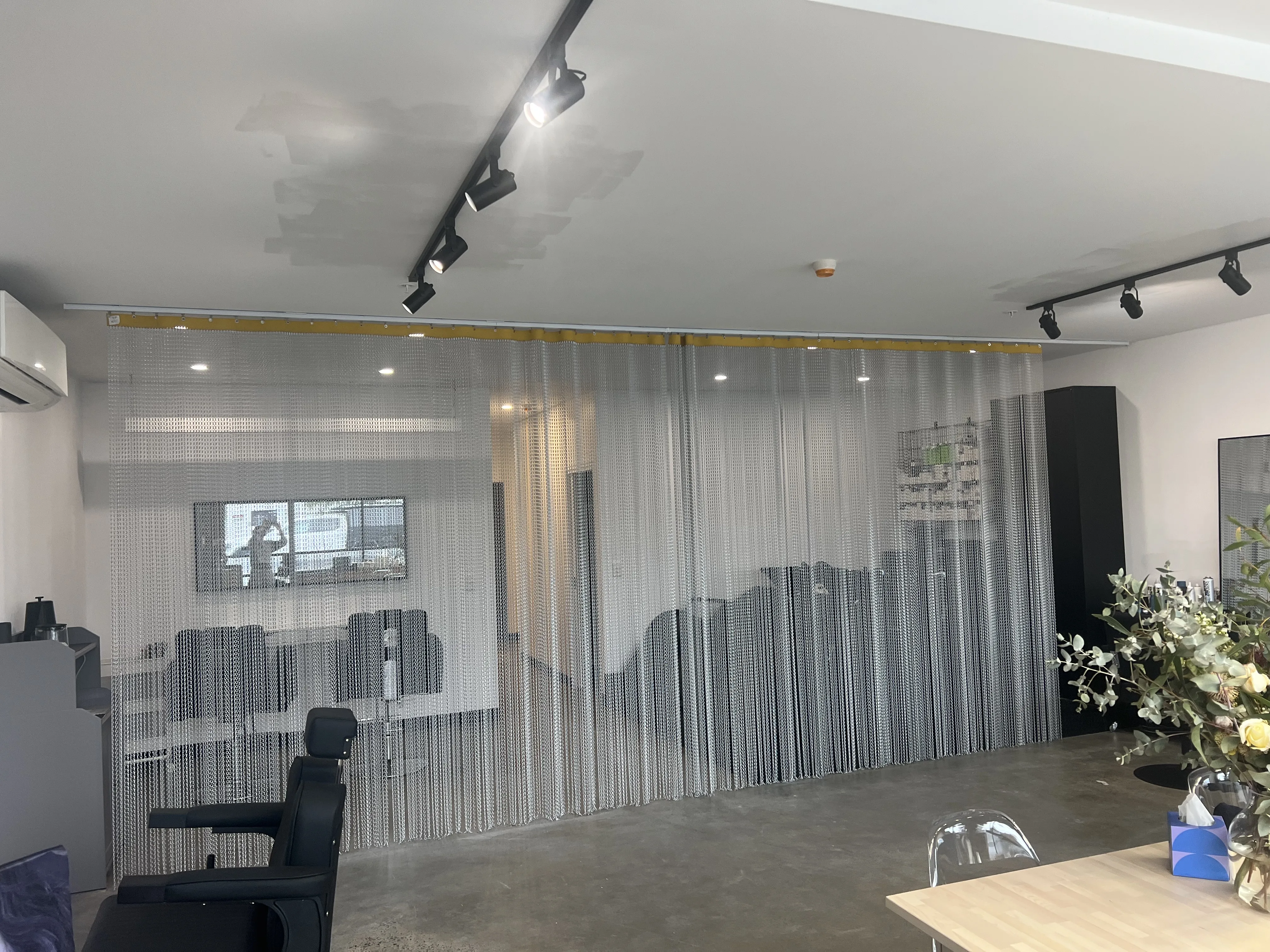 Tone Salon interior — silver chainmail mountain curtain, black styling chair, eucalyptus bouquet on polished concrete